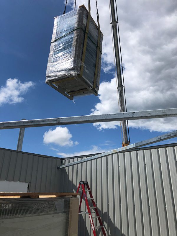 Crane lifting a packaged air conditioning plant onto a new-build commercial roof.