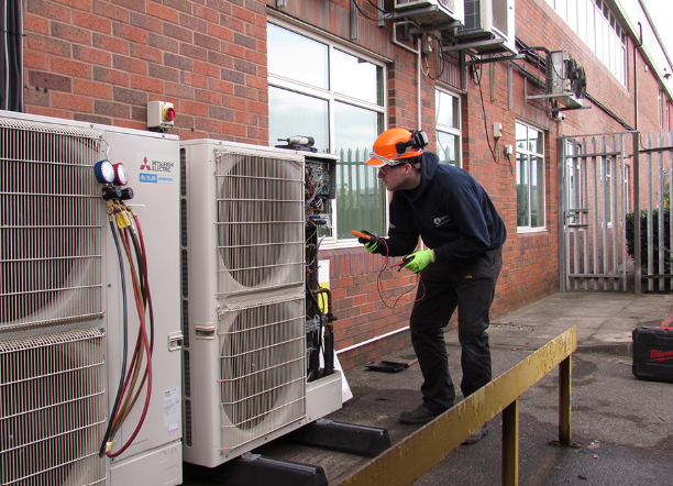 Universal Cooling engineer commissioning a Mitsubishi commercial air conditioning condenser unit on site.